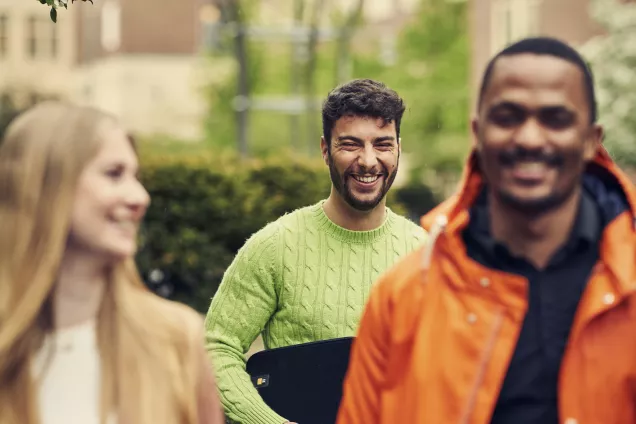 Tre leende studenter gåendes inne på Campus Helsingborgs innergård. Foto.